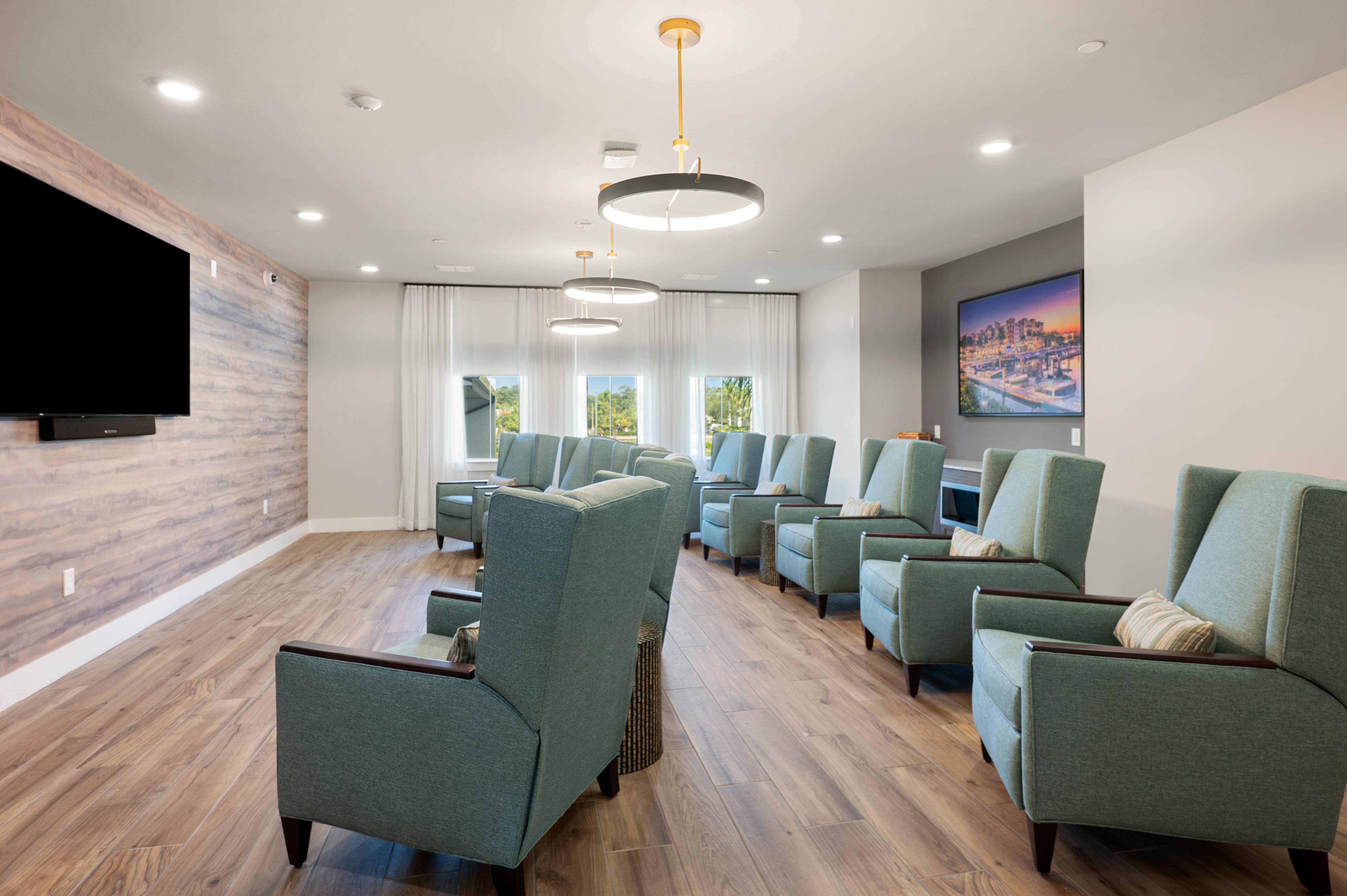 A living room with green chairs and a flat screen TV mounted on the wall.